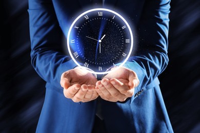 Image of Businessman holding virtual clock on dark background, closeup