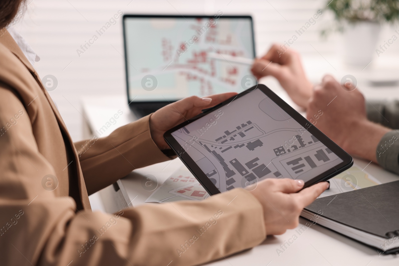 Photo of Cartographers working with cadastral maps at white table in office, closeup