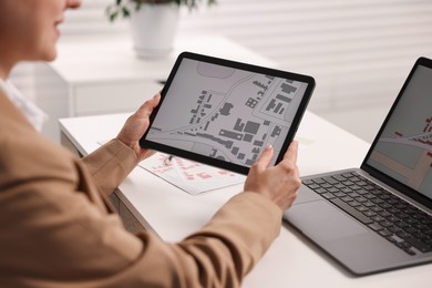 Cartographer working with cadastral map on tablet at white table in office, closeup