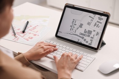Cartographer working with cadastral map on tablet at white table in office, closeup