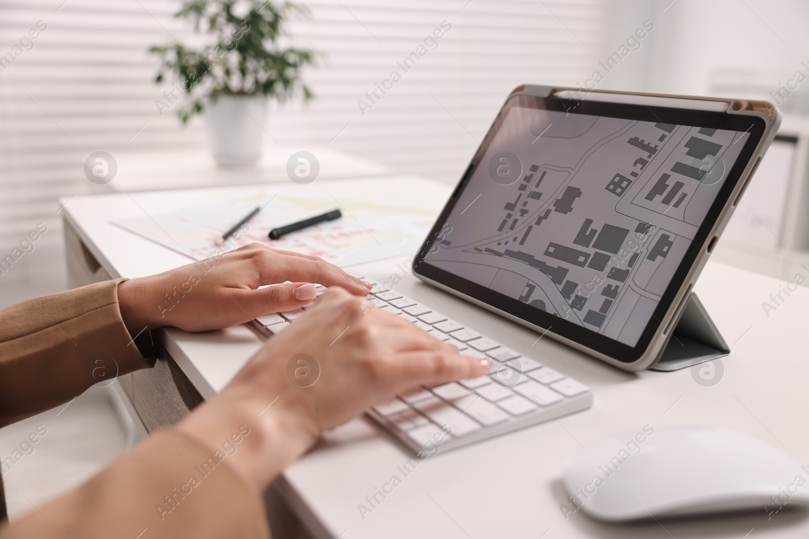 Photo of Cartographer working with cadastral map on tablet at white table in office, closeup