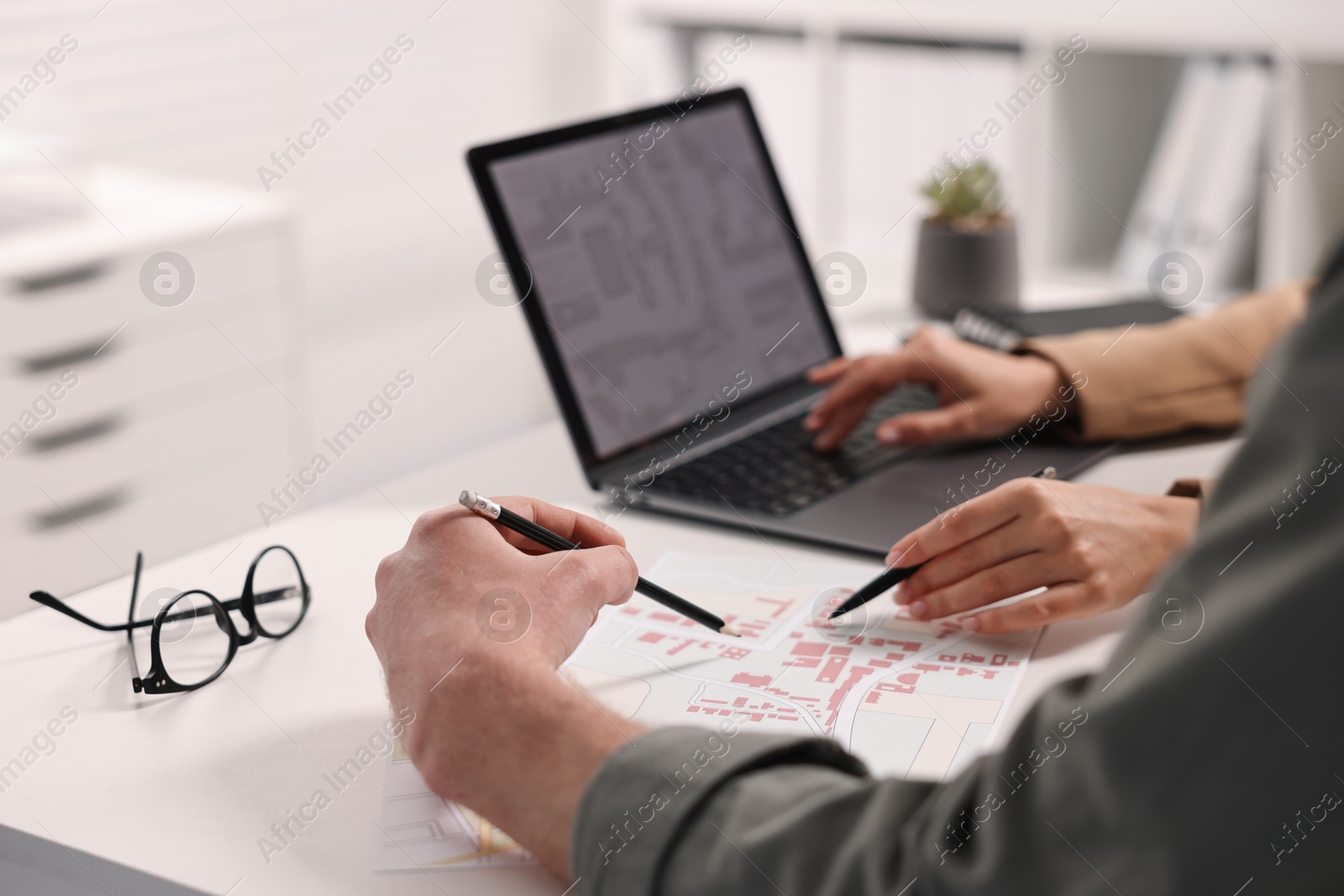 Photo of Cartographers working with cadastral map at white table in office, closeup