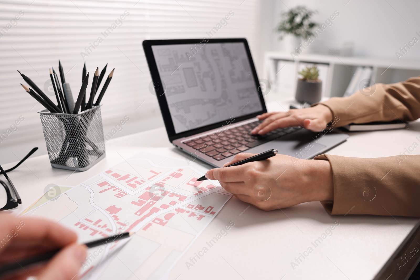 Photo of Cartographers working with cadastral maps at white table in office, closeup