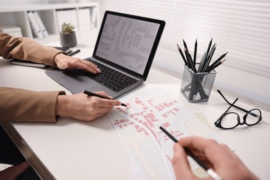 Photo of Cartographers working with cadastral maps at white table in office, closeup