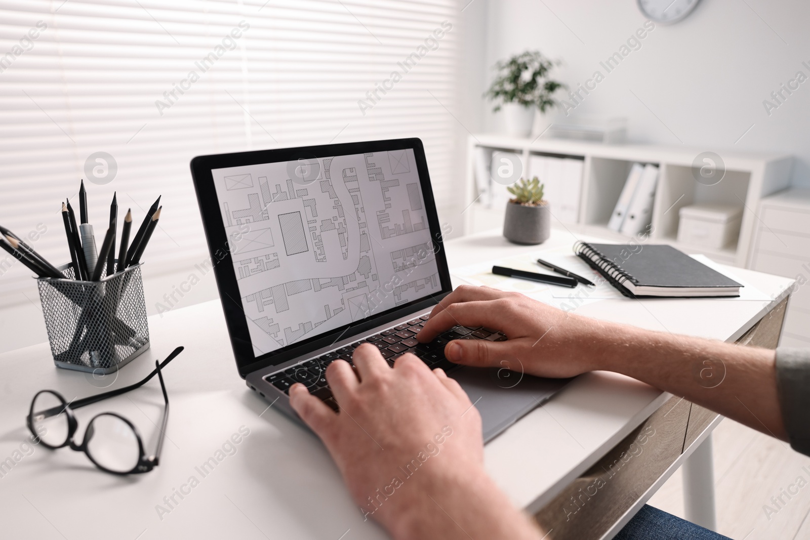 Photo of Cartographer working with cadastral map on laptop at white table in office, closeup