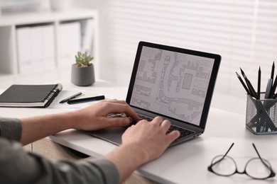 Photo of Cartographer working with cadastral map on laptop at white table in office, closeup