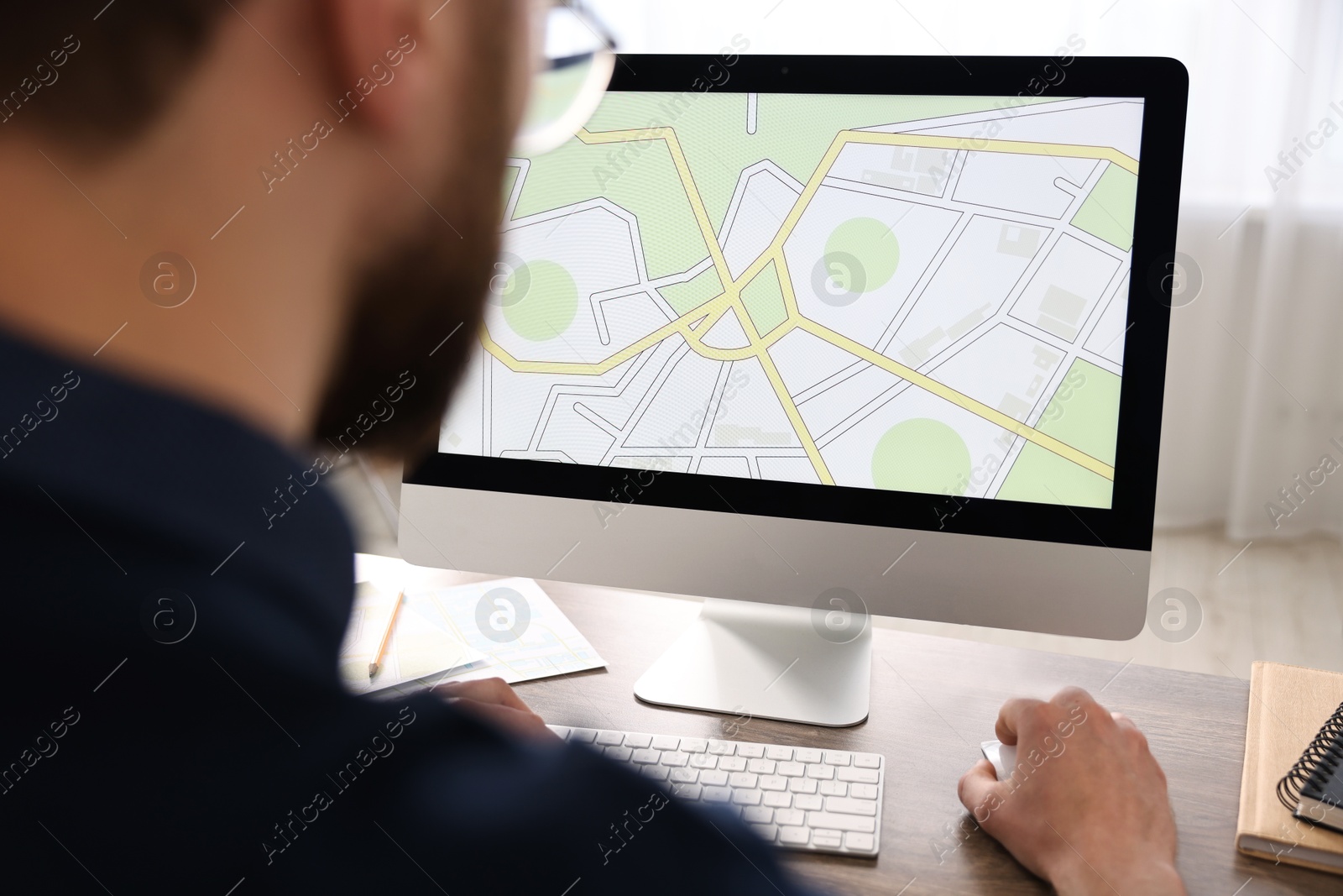 Photo of Cartographer working with cadastral map on computer at table in office, closeup