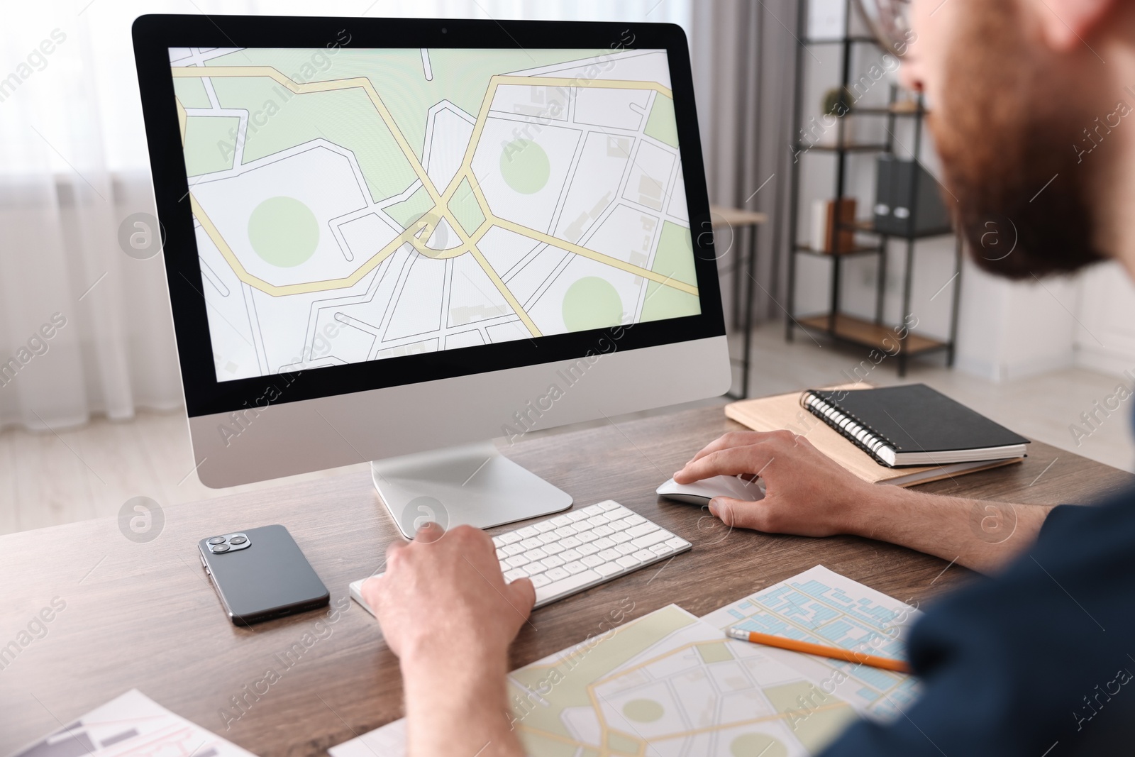 Photo of Cartographer working with cadastral map on computer at wooden table in office, closeup