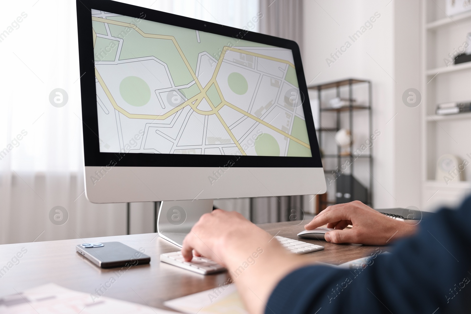 Photo of Cartographer working with cadastral map on computer at wooden table in office, closeup