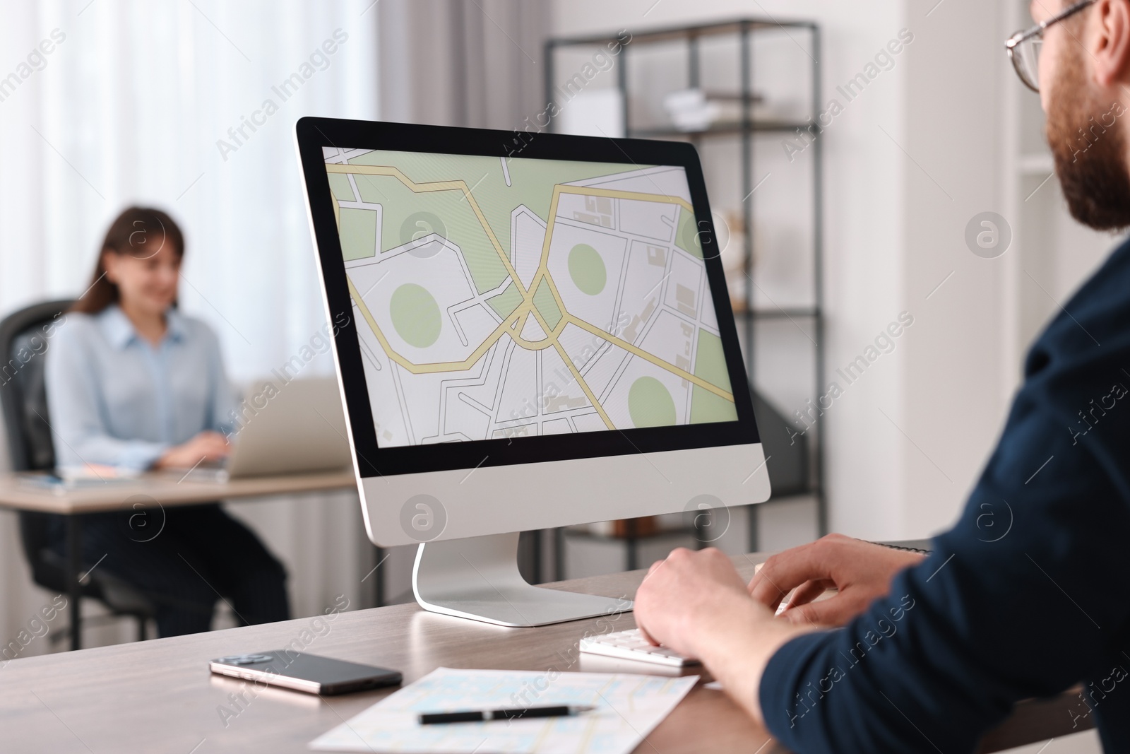 Photo of Cartographer working with cadastral map on computer at wooden table in office, closeup