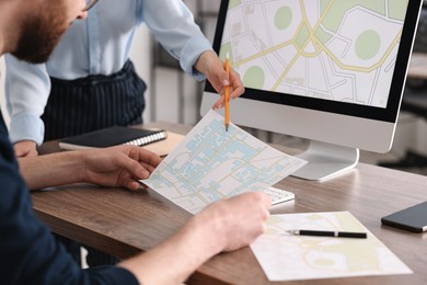 Cartographers working with cadastral maps at wooden table in office, closeup