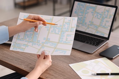 Photo of Cartographer working with cadastral maps at wooden table in office, closeup