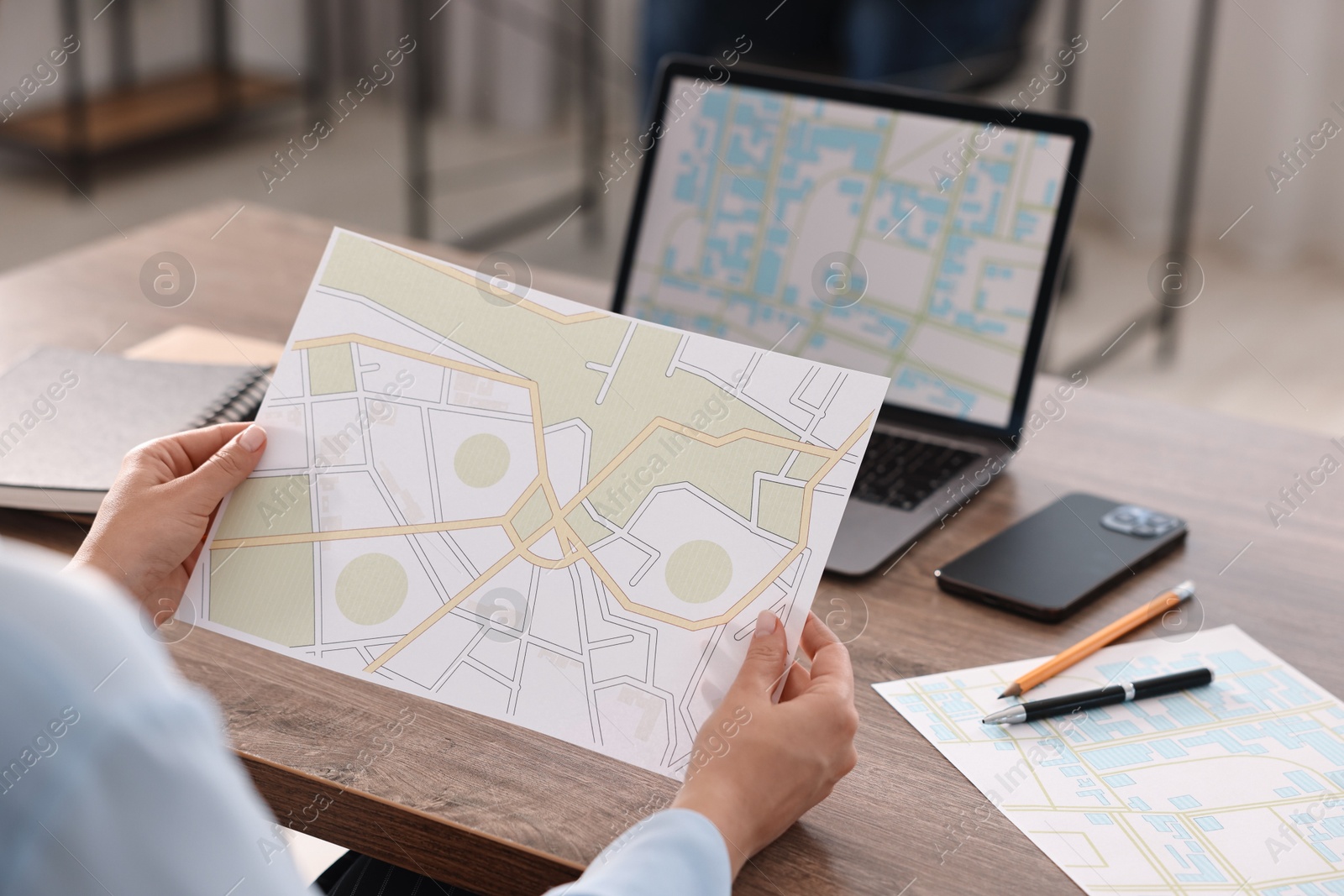 Photo of Cartographer working with cadastral maps at wooden table in office, closeup