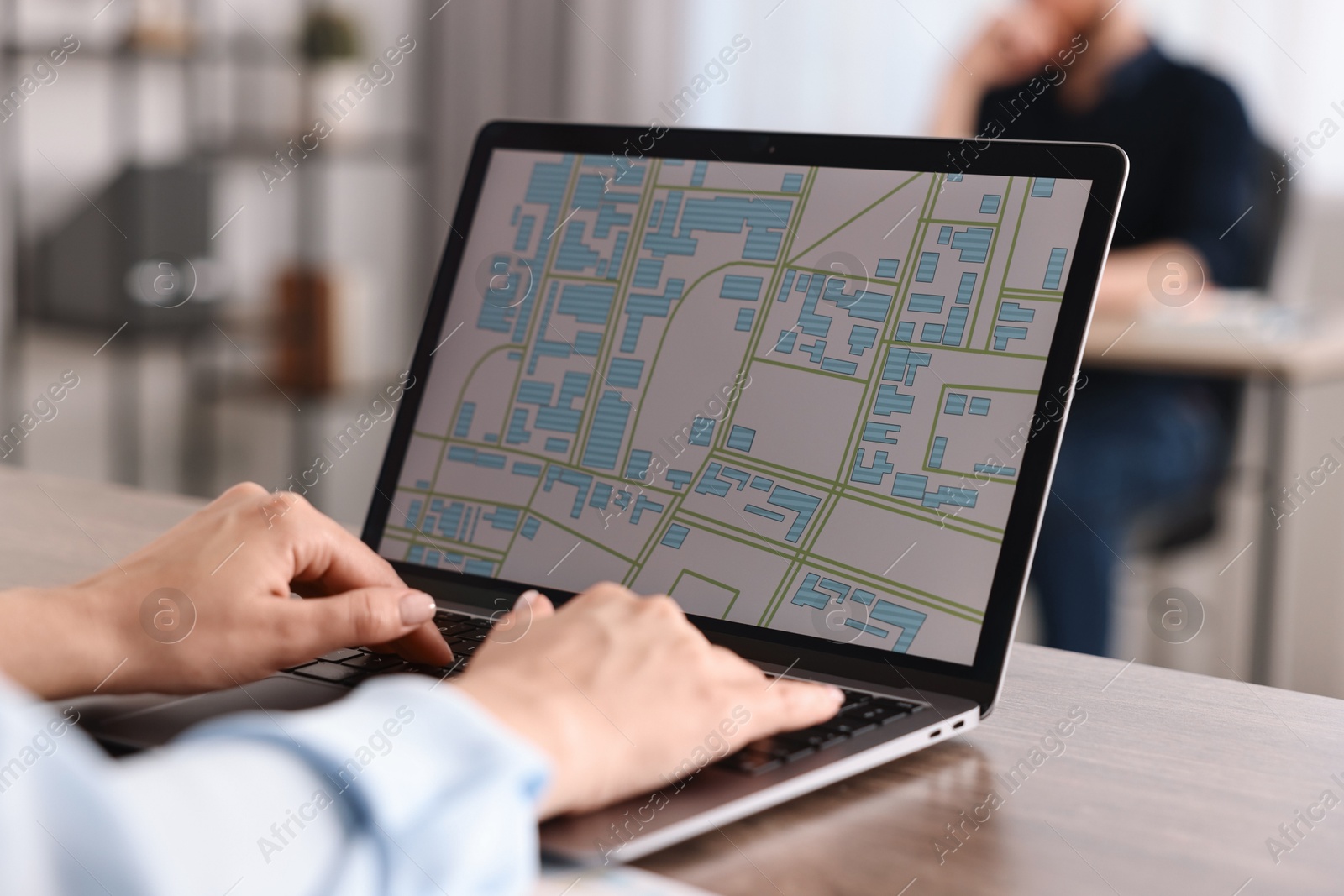 Photo of Smiling cartographer working with cadastral map on laptop at wooden table in office, closeup