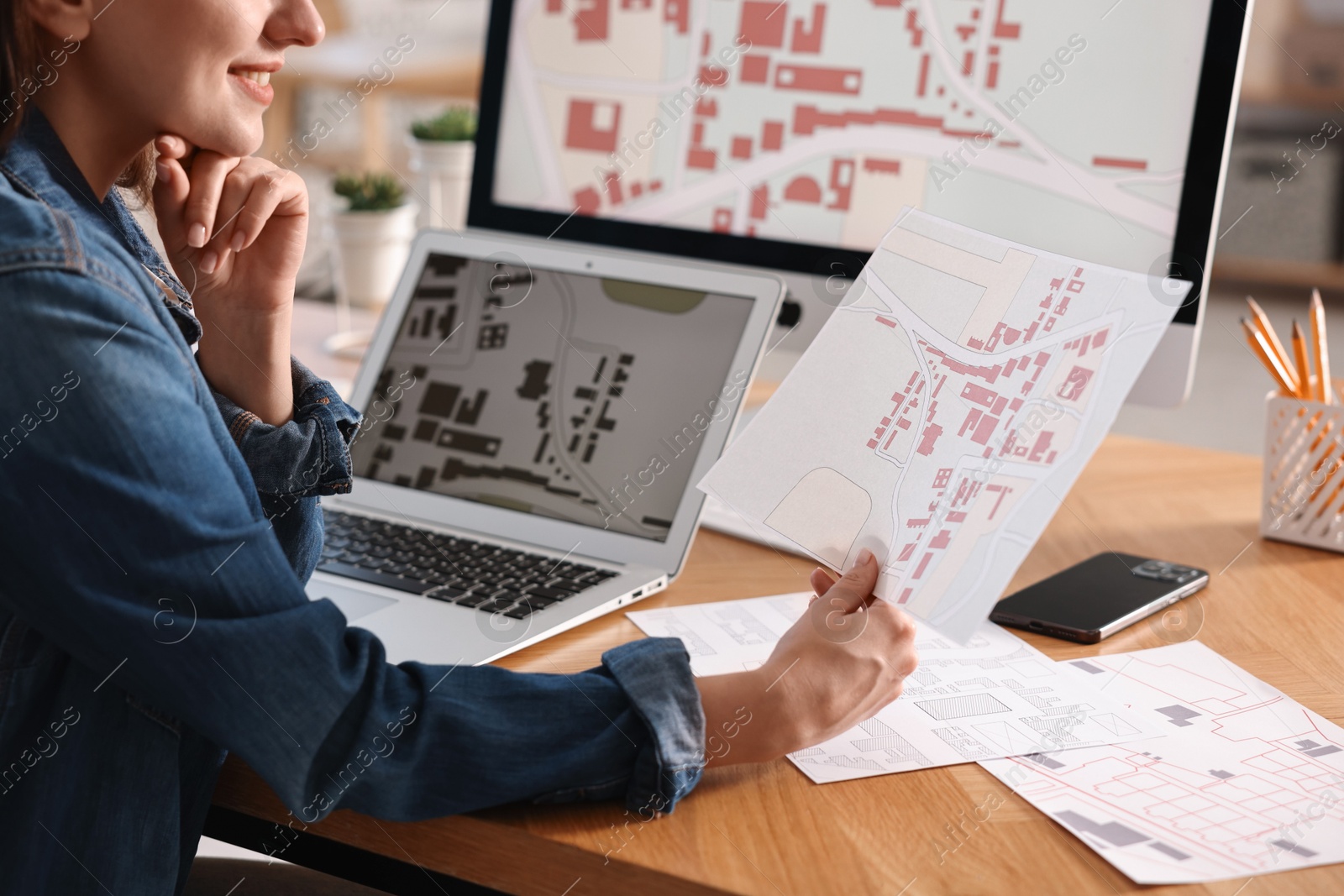 Photo of Smiling cartographer working with cadastral maps at wooden table in office, closeup