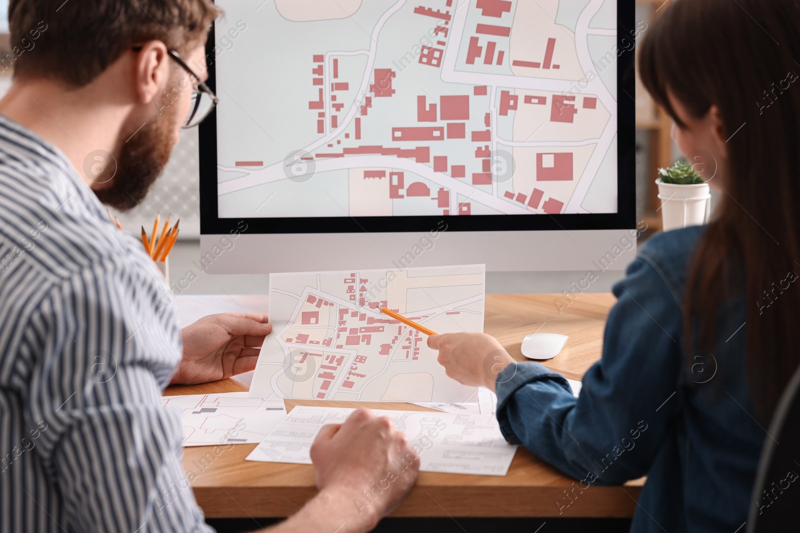 Photo of Cartographers working with cadastral maps at table in office, back view