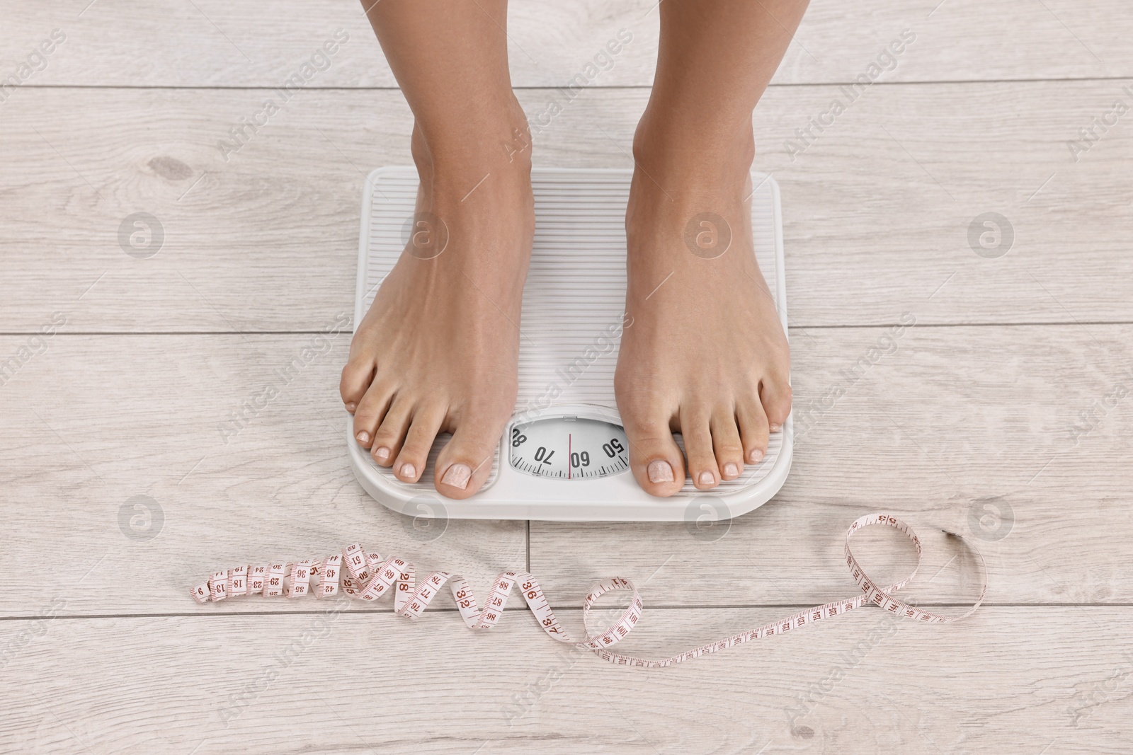 Photo of Woman standing on floor scale and measuring tape at home, top view