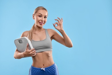 Photo of Happy woman with floor scale showing ok gesture on light blue background. Space for text