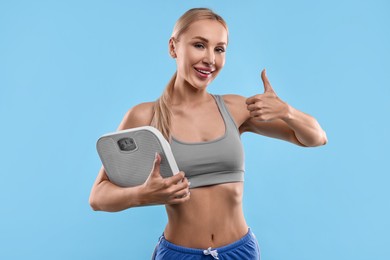 Photo of Happy woman with floor scale showing thumb up on light blue background