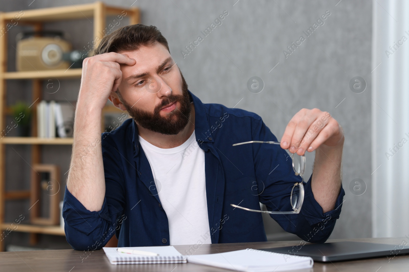 Photo of Overwhelmed man sitting with glasses at table indoors