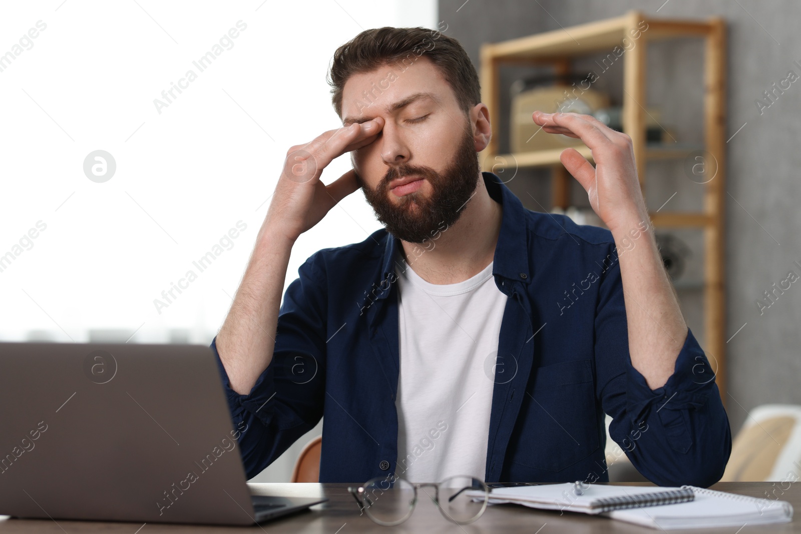 Photo of Overwhelmed man sitting with laptop at table indoors