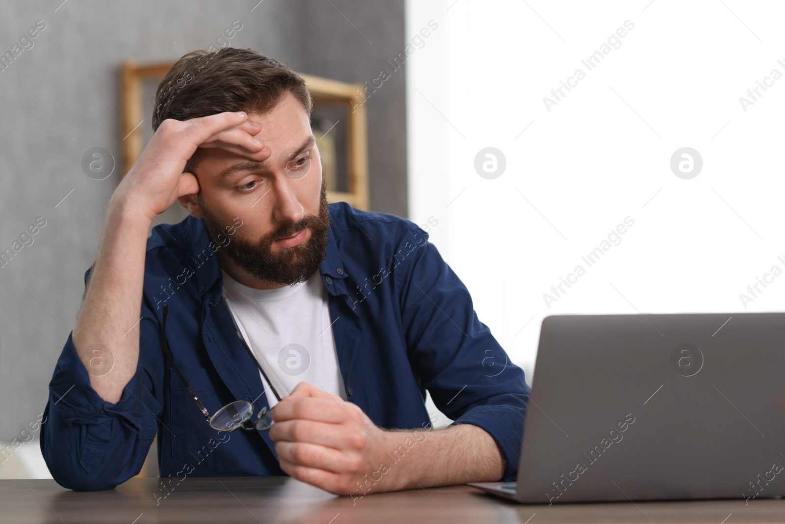 Photo of Overwhelmed man sitting with laptop at table indoors