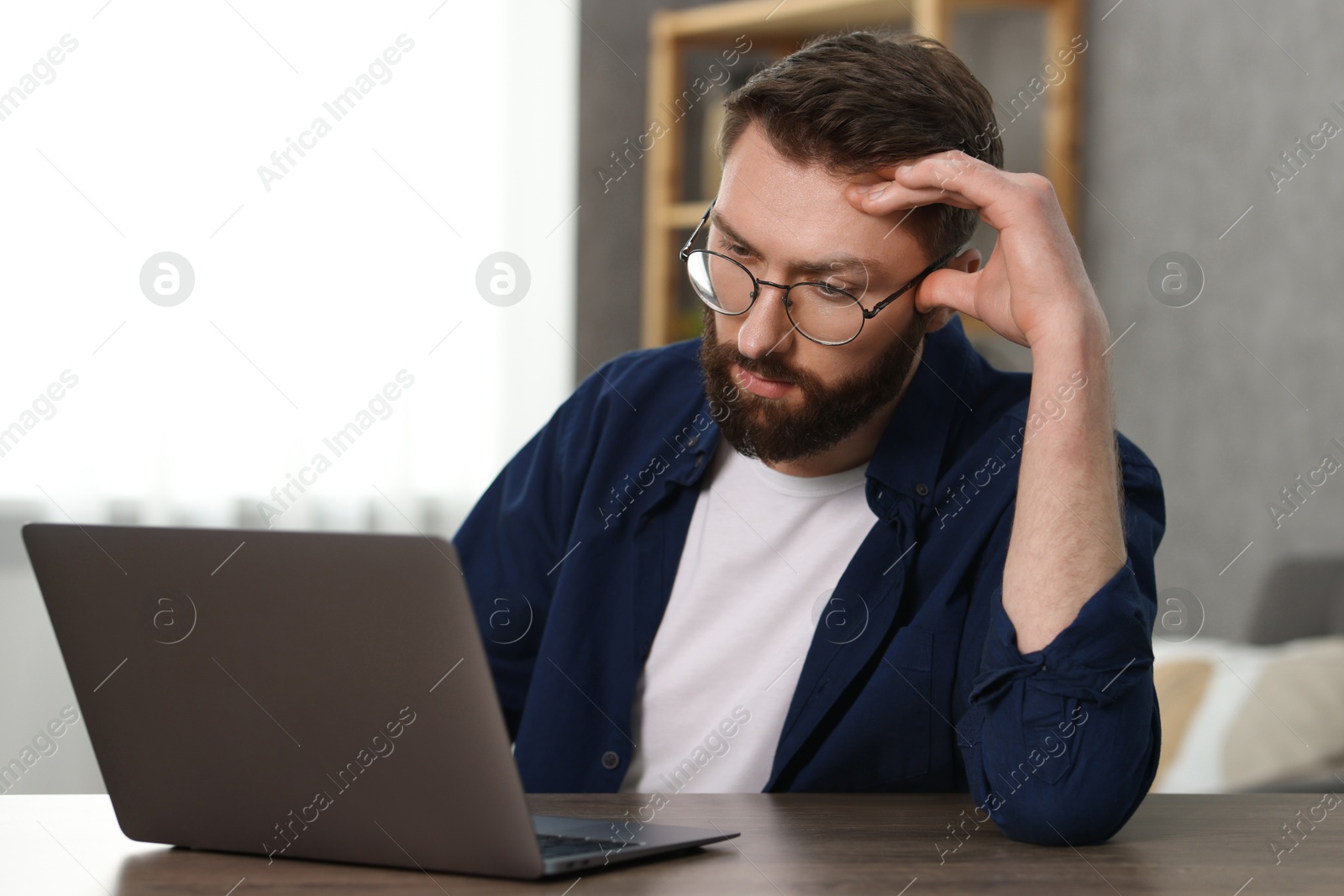 Photo of Overwhelmed man sitting with laptop at table indoors