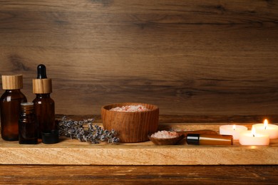 Different aromatherapy products and burning candles on wooden table