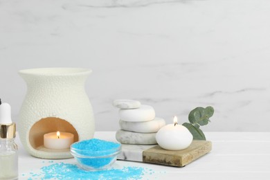 Different aromatherapy products and burning candles on white wooden table