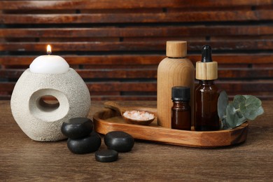 Different aromatherapy products and burning candle on wooden table