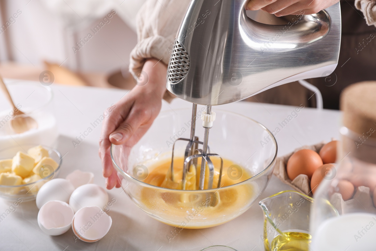 Photo of Woman making dough with mixer in bowl at table, closeup