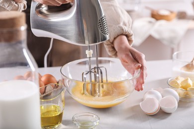 Photo of Woman making dough with mixer in bowl at table, closeup