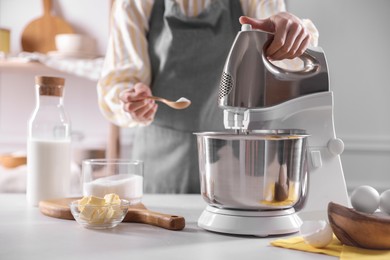 Photo of Woman adding sugar into bowl of stand mixer while making dough at table indoors, closeup