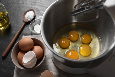 Making dough. Raw eggs in bowl of stand mixer and ingredients on black table, closeup