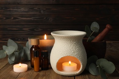 Photo of Aromatherapy. Scented candles, bottles and eucalyptus branches on wooden table, closeup