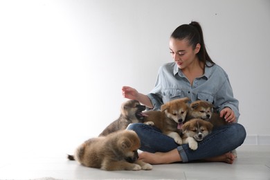 Woman with Akita Inu puppies sitting on floor near light wall. Space for text