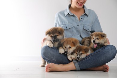 Photo of Woman with Akita Inu puppies sitting on floor near light wall, closeup. Space for text