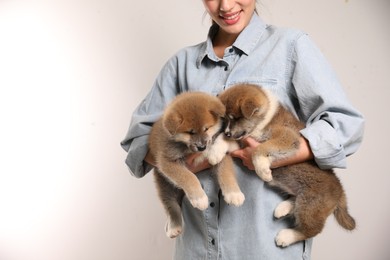 Photo of Woman holding Akita Inu puppies on light background, closeup. Space for text