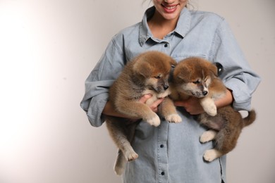 Woman holding Akita Inu puppies on light background, closeup. Space for text