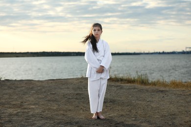 Cute little girl in kimono practicing karate near river