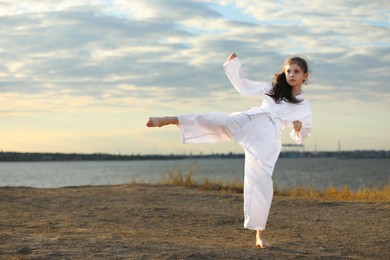 Photo of Cute little girl in kimono practicing karate near river