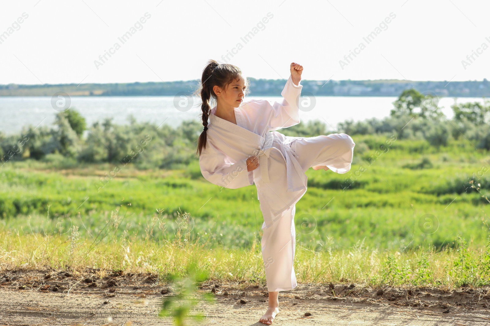 Photo of Cute little girl in kimono practicing karate outdoors