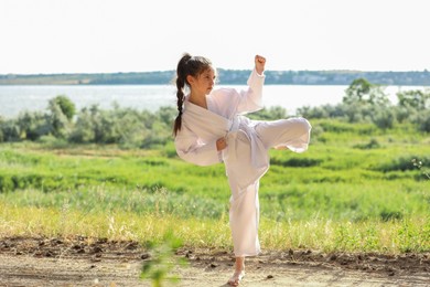 Photo of Cute little girl in kimono practicing karate outdoors