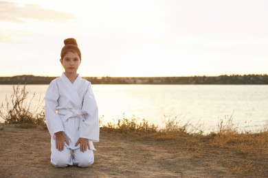 Photo of Cute little girl in kimono meditating near river at sunset. Karate practicing