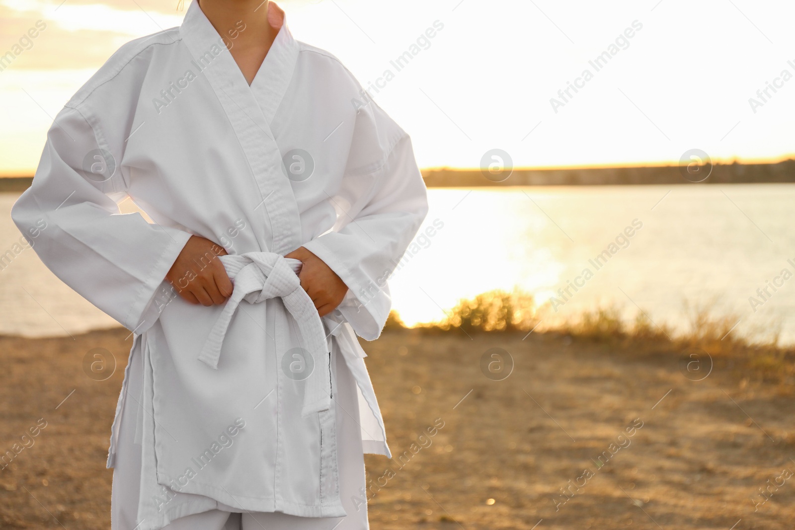 Photo of Cute little girl in kimono near river at sunset, closeup. Karate practicing