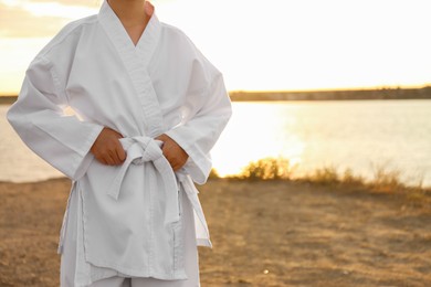 Cute little girl in kimono near river at sunset, closeup. Karate practicing