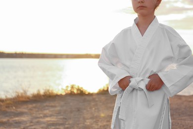 Photo of Cute little girl in kimono near river at sunset, closeup. Karate practicing