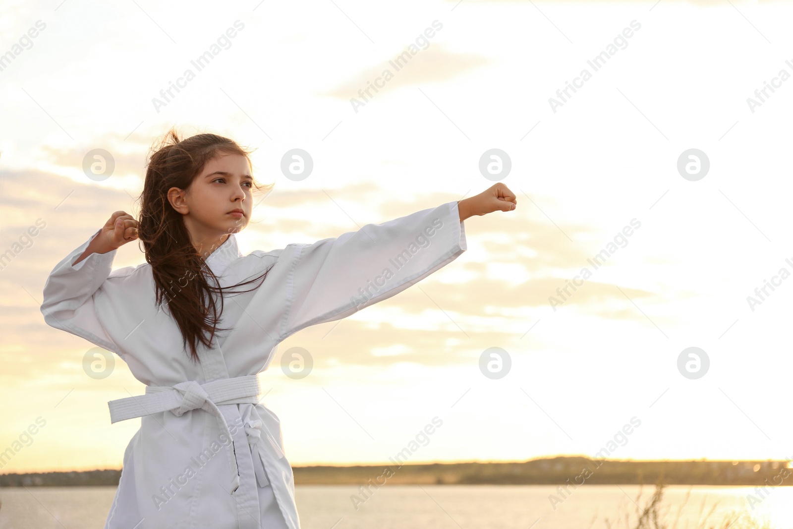 Photo of Cute little girl in kimono practicing karate near river at sunset