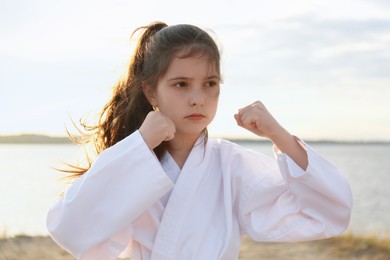 Photo of Cute little girl in kimono practicing karate near river on sunny day