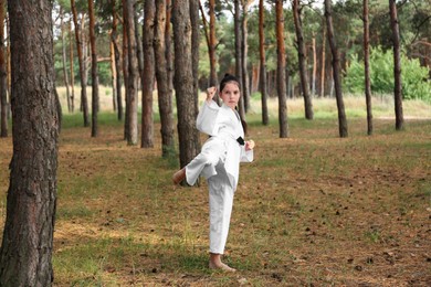 Cute little girl in kimono practicing karate in forest